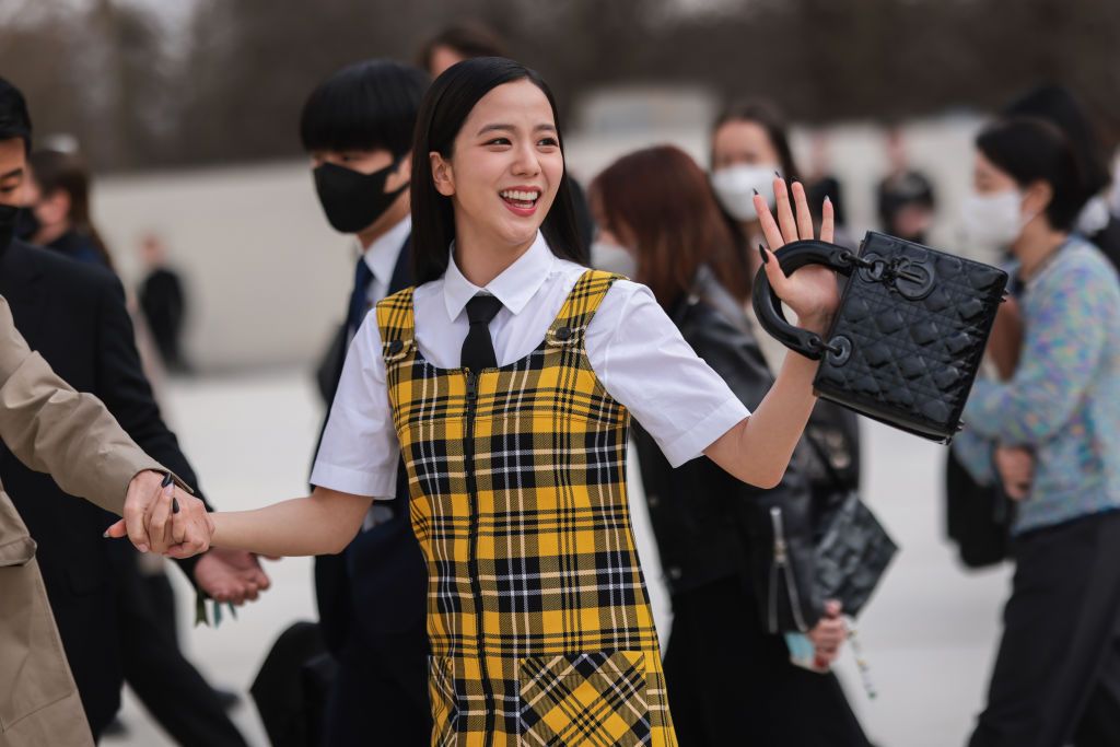 PARIS, FRANCE - MARCH 01: Kim Ji-soo aka Jisoo from Blackpink wears a white shirt from Dior, a black tie from Dior, a gray blazer jacket from Dior ,a white / yellow / black checkered print pattern tank-top / zipper / short dress, a black shiny leather varnished leather Lady D-Lite hand bag from Dior, outside Dior, during Paris Fashion Week - Womenswear F/W 2022-2023, on March 01, 2022 in Paris, France. (Photo by Jeremy Moeller/Getty Images)