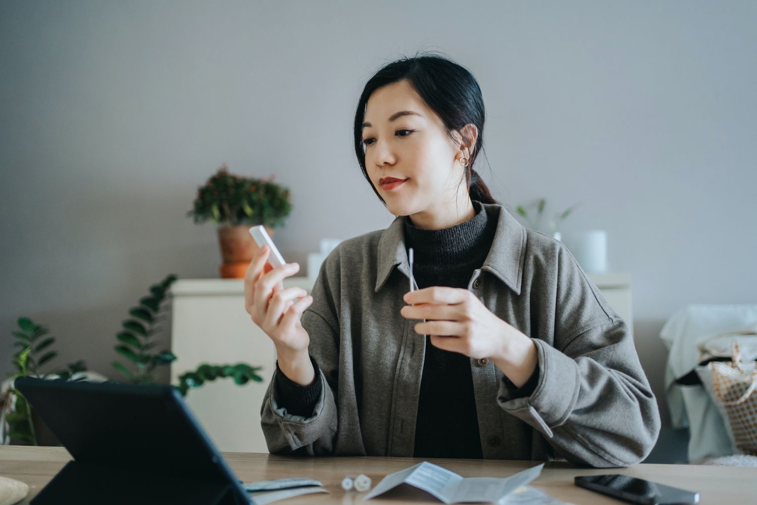 Young Asian woman holding a Covid-19 rapid lateral flow test kit and a nasal swab, carrying out a Coronavirus rapid self test at home. She is having a video call appointment on digital tablet with her family doctor for advice and consultation