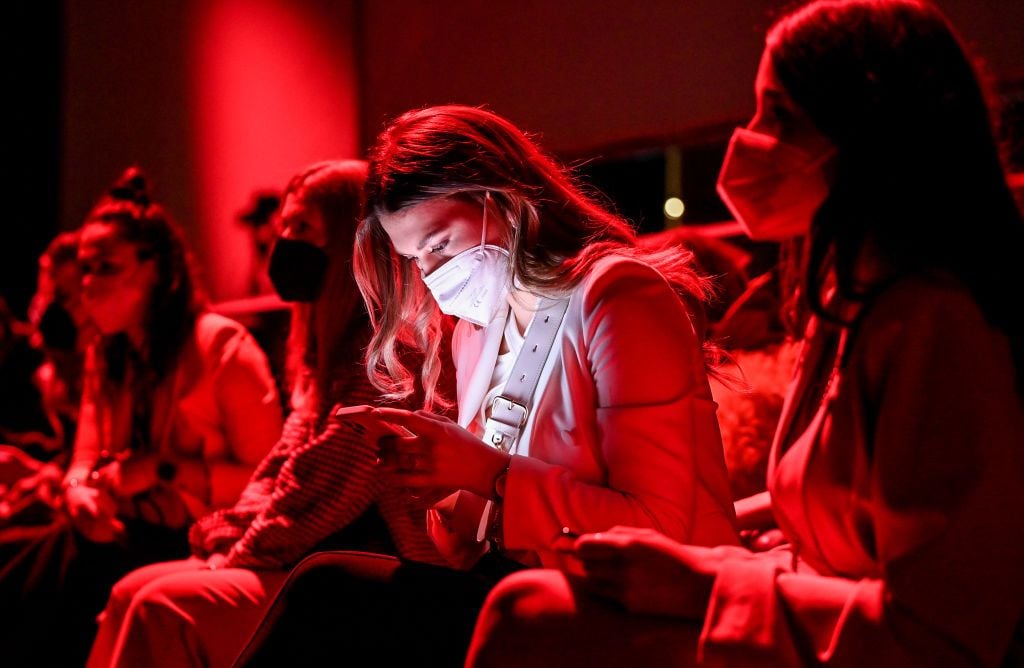 16 March 2022, Berlin: Berlin Fashion Week: Guests sit at the Mercedes-Benz Fashion Week before the show of designer Danny Reinke at Kraftwerk in red light and are partially illuminated by the light of their smartphones. Berlin Fashion Week runs from March 14 to 20. Photo: Jens Kalaene/dpa-Zentralbild/dpa (Photo by Jens Kalaene/picture alliance via Getty Images)