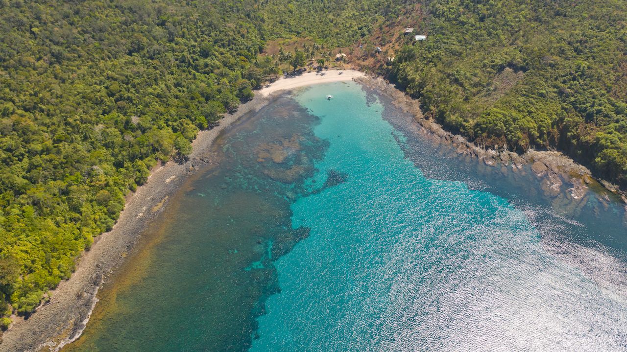 Sea bay with turquoise water and a small white beach.Coast of the island of Camiguin, Philippines.Beautiful lagoon and volcanic island covered with dense forest, view from above.