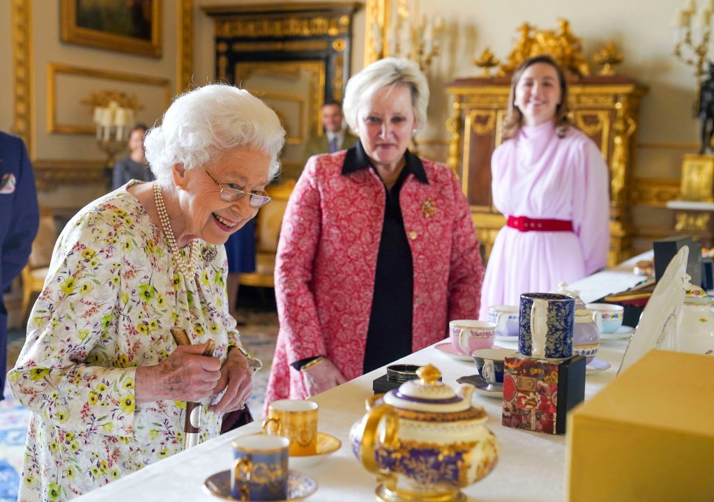 WINDSOR, ENGLAND - MARCH 23: Queen Elizabeth II talks to Pamela Harper (centre) from British craftwork company, Halcyon Days as she views a display of artefacts to commemorate the company's 70th anniversary in the White Drawing Room at Windsor Castle, on March 23, 2022 in Windsor, England. The Queen viewed a selection of hand-decorated archive enamelware and fine bone china, including their earliest designs from the 1950s. (Photo Steve Parsons - WPA Pool/Getty Images)