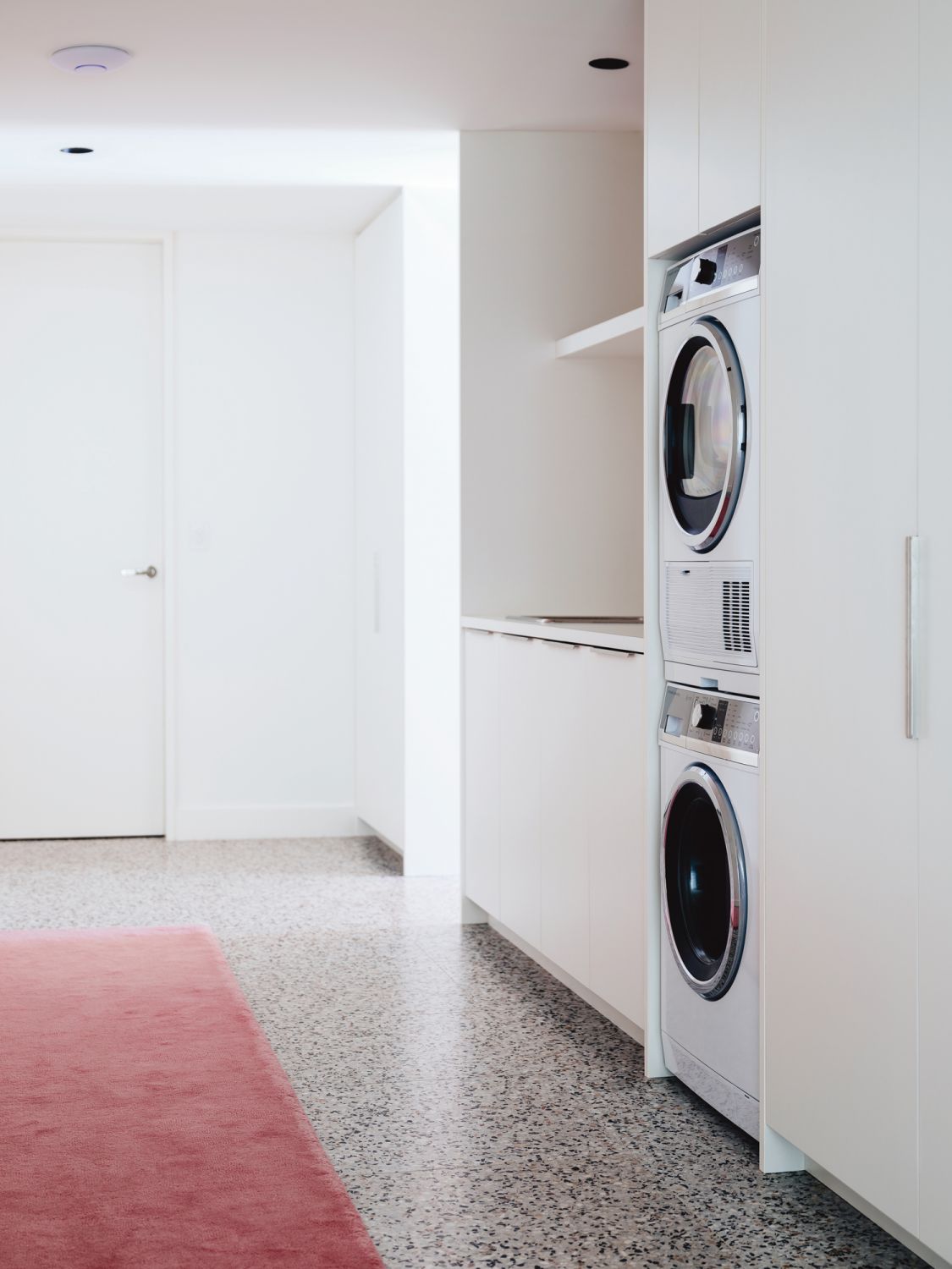 Laundry machines from Fisher & Paykel are housed beside sleek white cabinetry in the hallwa