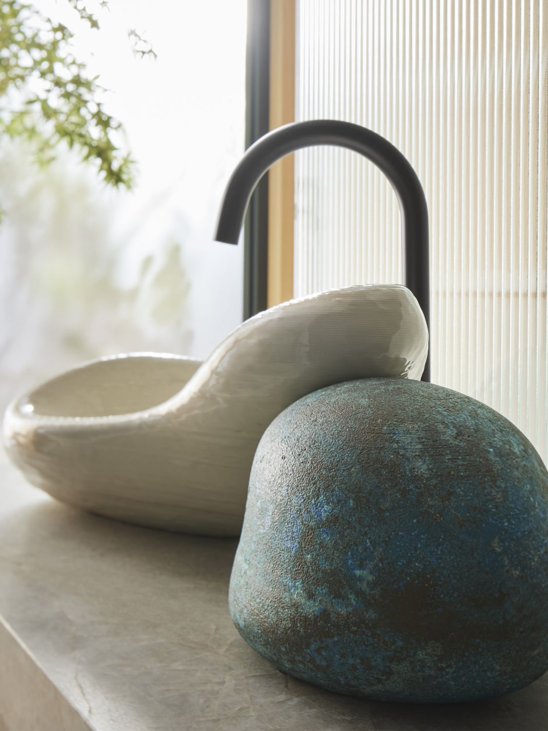The asymmetric vitreous china basin slumps over a hand-poured brass ‘rock’ with a patina finish