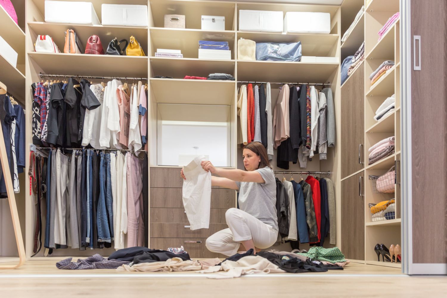 Young woman throwing clothes in walk in closet. Mess in wardrobe and dressing room concept