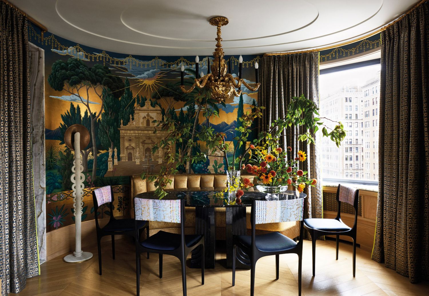 A De Gournay Sicilian scene wallpaper in a custom finish, coupled with a gold chandelier overhead, sets an opulent mood in the dining room