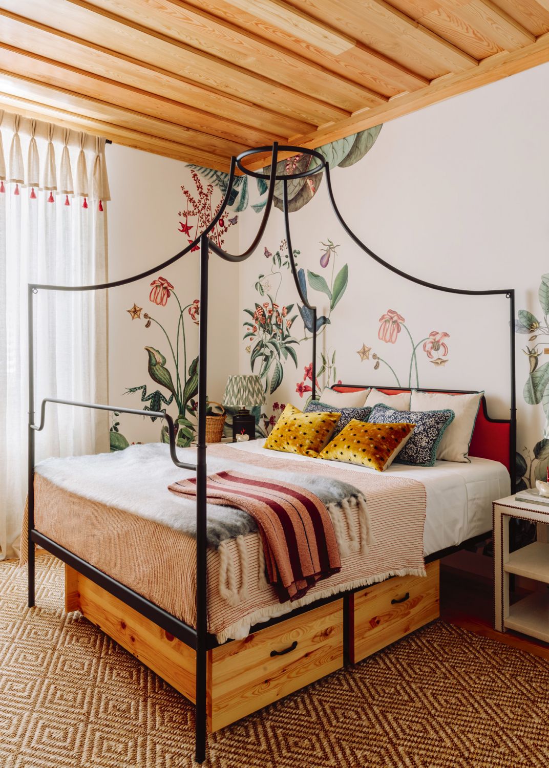 The botanical wallpaper, coupled with the unusual bed frame and tasselled curtains contribute to this bedroom’s whimsical look