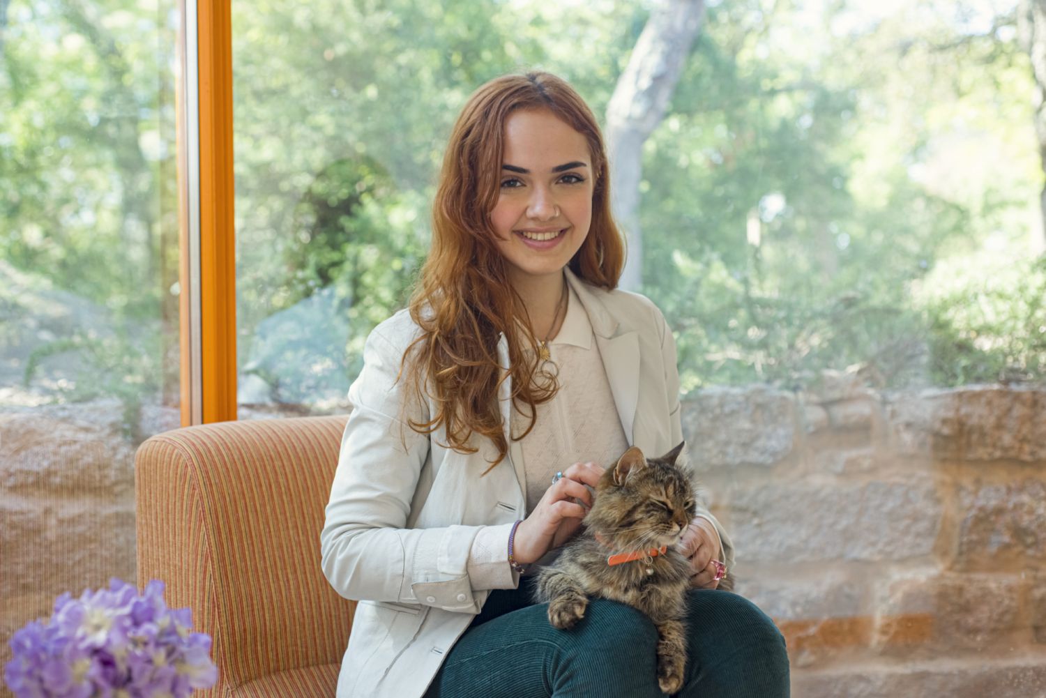 Portrait of a young woman with her cat sitting on the armchair in her living room