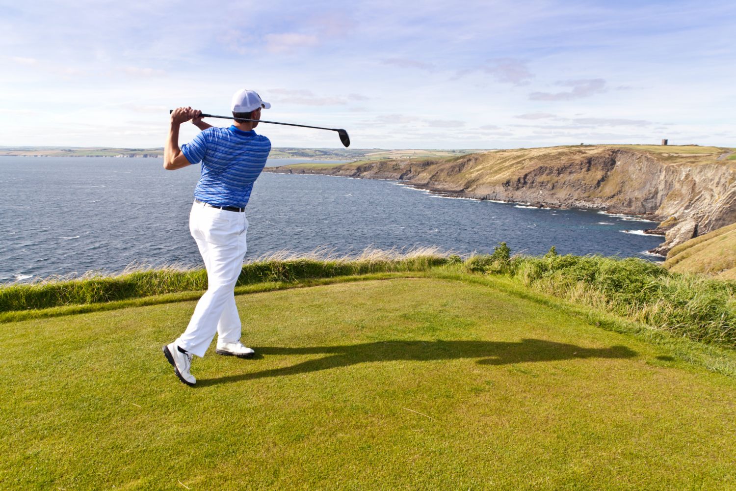 Golfer on a tee box overlooking the ocean driving off at a cliff edged hole.