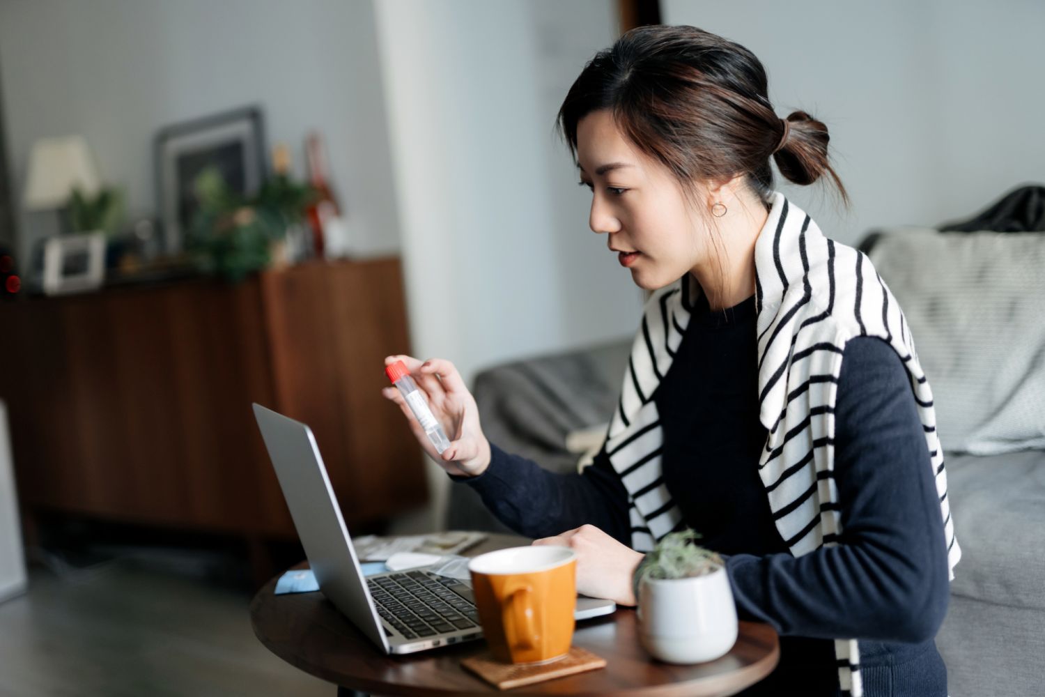 Young Asian woman consulting to her family doctor online in a virtual appointment, holding a medical test tube, conducting Covid-19 diagnostic test at home