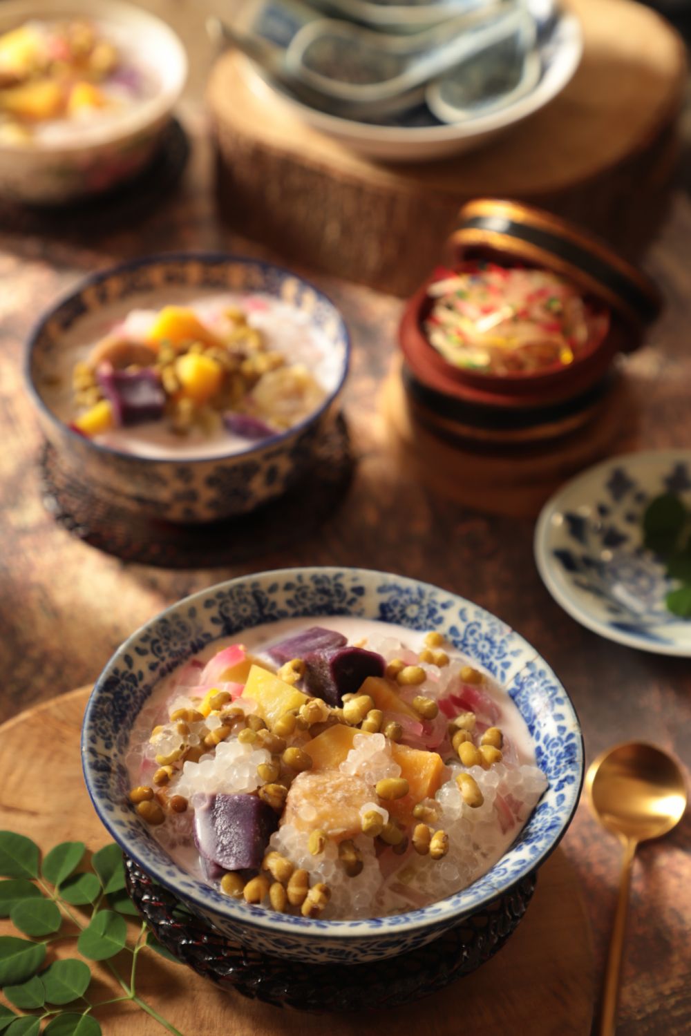 Bubur Cha Cha, a popular Peranakan dessert in Malaysia and Singapore. Sweet potatoes, bananas, beans, sago and tapioca pearls in sweet coconut milk soup. Served in a vintage bowl of Oriental pattern. Placed on a rustic table with another portions, also in vintage bowl and vintage soup spoons.