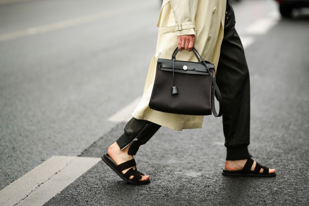 PARIS, FRANCE - JUNE 25: Lukas Osiecki wears a pale yellow long trench coat, black satin sport pants, a black shiny leather and fabric handbag from Hermes, black suede Chypre sandals from Hermes , outside the Hermes show, during Paris Fashion Week - Menswear Spring/Summer 2023, on June 25, 2022 in Paris, France. (Photo by Edward Berthelot/Getty Images)
