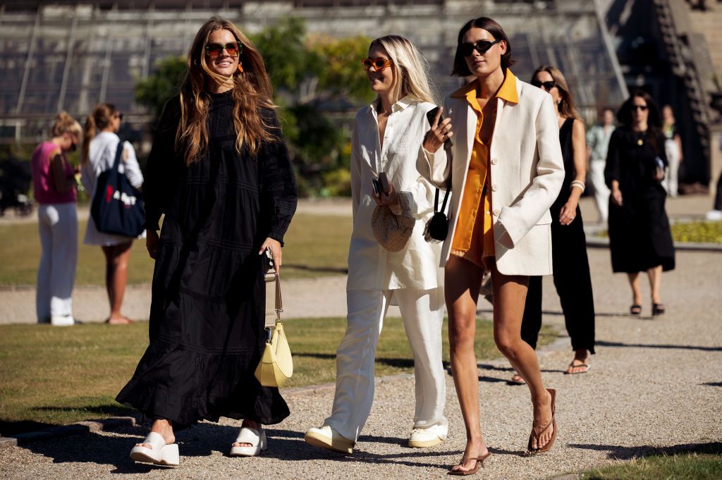 COPENHAGEN, DENMARK - AUGUST 10: Lois Schindeler wearing long black maxi dress, orange sunglasses, white shoes and pale yellow bag and Frederika Ekerot wearing white pants, white long shirt, beige bag, white sneakers and light brown sunglasses and Vera Vanerup wearing orange shirt, light orange knitted shorts, white jacket, brown bag and brown slippers posing outside Skall Studio during Copenhagen fashion week Spring / Summer 2023on August 10, 2022 in Copenhagen, Denmark. (Photo by Raimonda Kulikauskiene/Ge