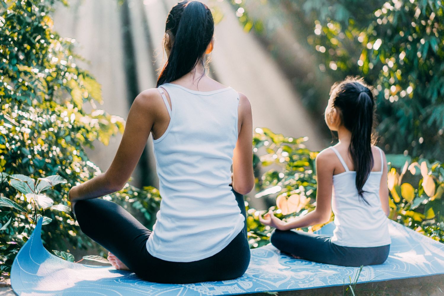 Asian mother and daughter meditating in lotus position in rainforest in Bali, Indonesia