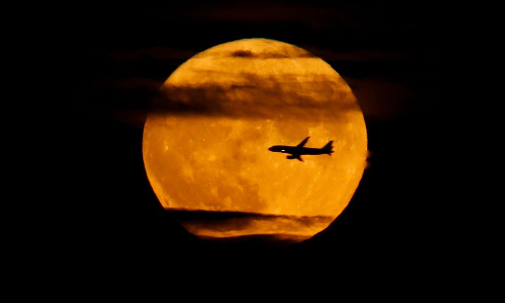 WEST ORANGE, NJ - AUGUST 11: An airplane flies past the full Sturgeon Supermoon as it rises above New York City on August 11, 2022, as seen from West Orange, New Jersey. (Photo by Gary Hershorn/Getty Images)