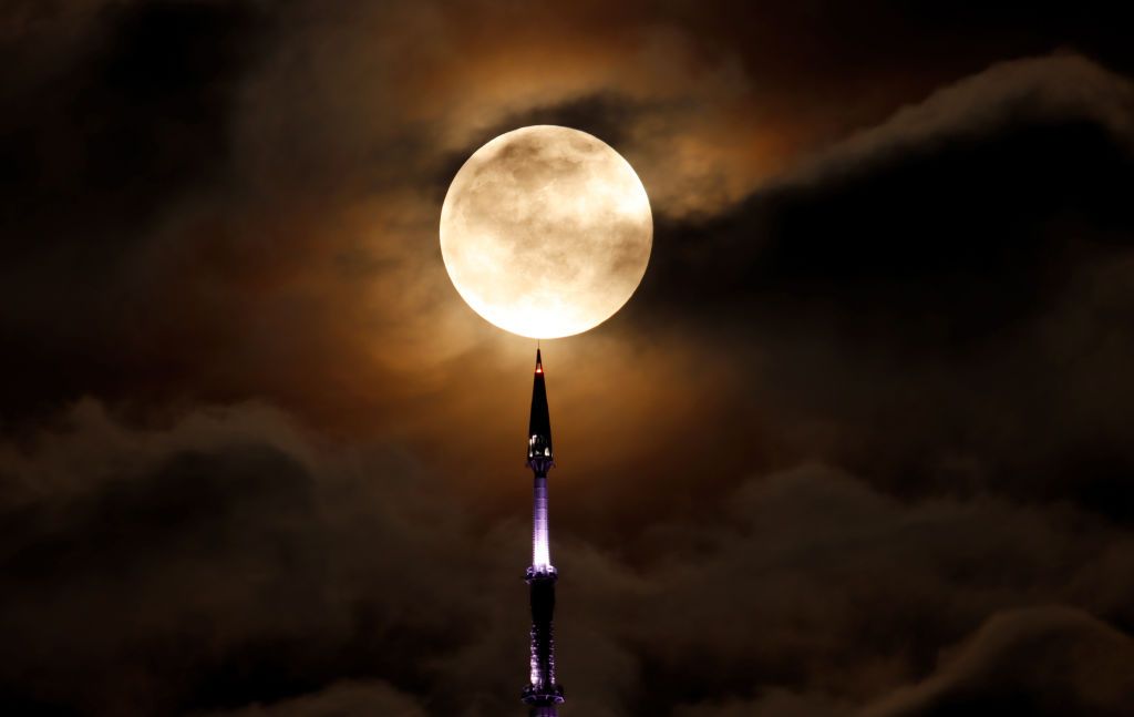 JERSEY CITY, NJ - MAY 15: The full Super Flower Moon rises behind the antenna on top of One World Trade Center in New York City before the start of a lunar eclipse on May 15, 2022, as seen from Jersey City, New Jersey. (Photo by Gary Hershorn/Getty Images)