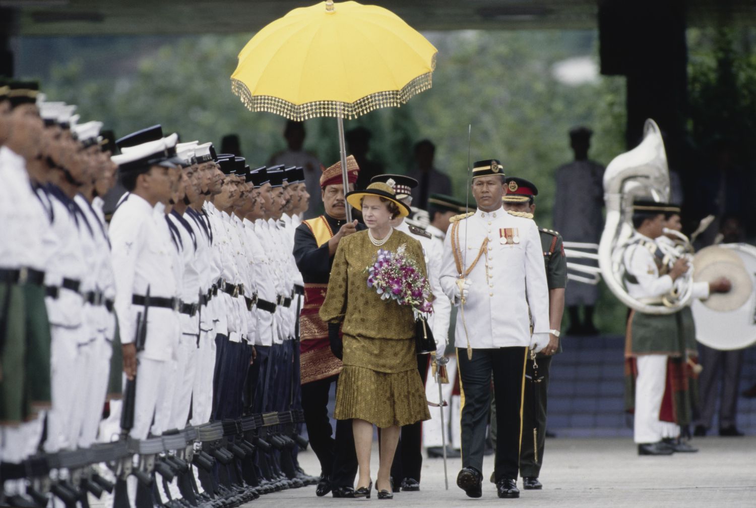 British Royal Queen Elizabeth II, wearing a black-and-gold outfit with a matching Philip Somerville hat, during a military inspection while visiting the Sultan Salahuddin Abdul Aziz Mosque, in Shah Alam, Selangor, Malaysia, 14th October 1989. The Queen is in Malaysia to open the Commonwealth Heads of Government Meeting on 18th October. (Photo by Tim Graham Photo Library via Getty Images)