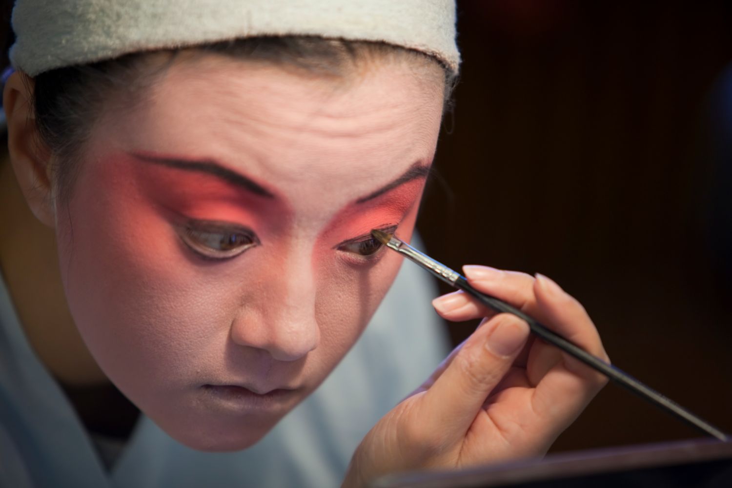 A Chinese opera performer lines their eyes with dark liner