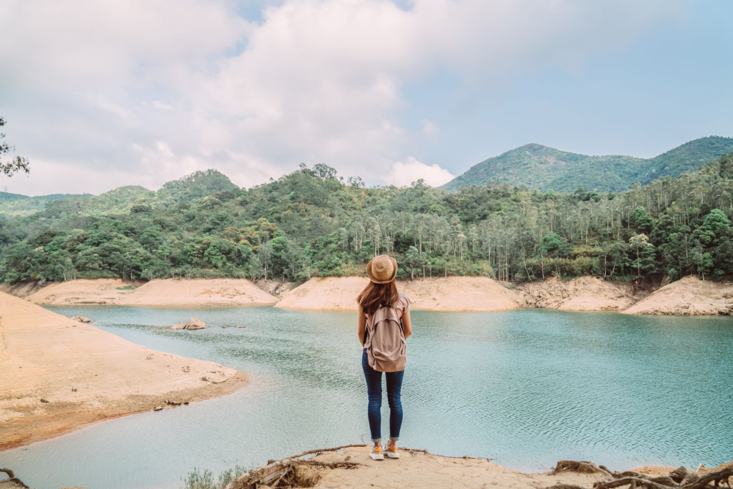 Rear view of young pretty woman enjoying a scenic beautiful lake view joyfully while she is hiking on nature trail.
