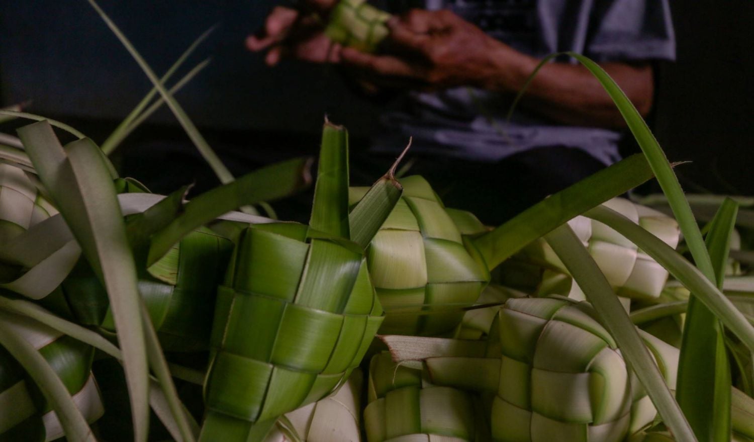 BOGOR, INDONESIA - APRIL 29 2022: Indonesian vendors weave palm leaves used to make traditional rice cakes known as 'Ketupat' in preparation of the upcoming Eid al-Fitr in Bogor, West Java, Indonesia on April 29, 2022.