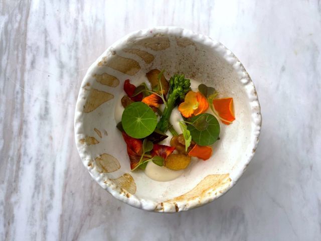 Su's charred kailan stems are served with local herbs atop over-fermented petai tempeh, garlic sour cream, and jalapeño ketchup