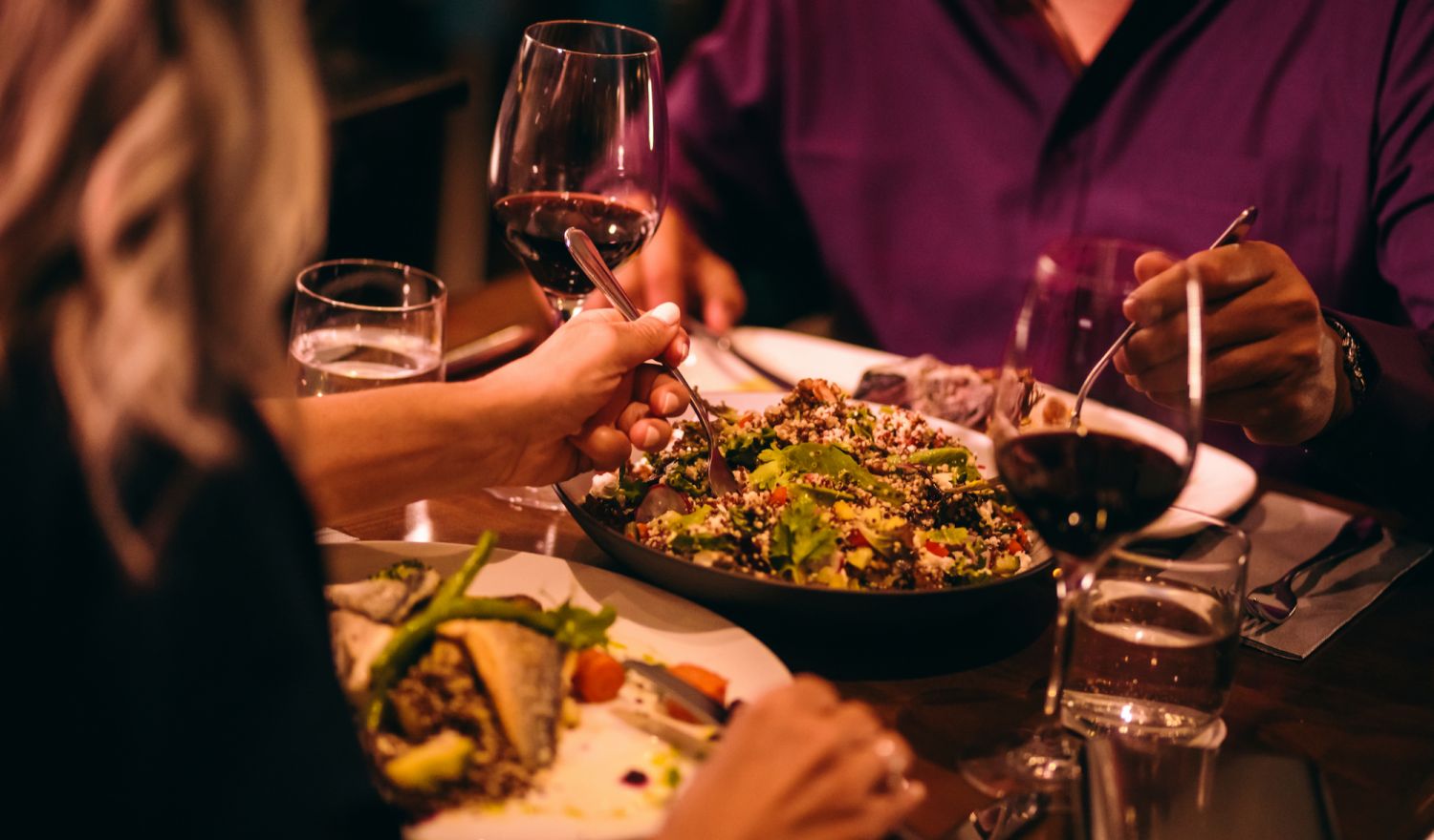 Couple on dinner date night eating healthy food with quinoa salad and drinking red wine