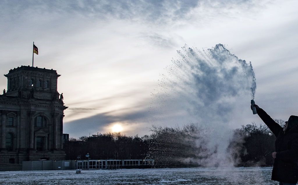 01 February 2021, Berlin: On the lawn in front of the Reichstag, a man hurls boiling water from a bottle into the air, which immediately freezes in the sub-zero temperatures. Photo: Paul Zinken/dpa-Zentralbild/ZB (Photo by Paul Zinken/picture alliance via Getty Images)
