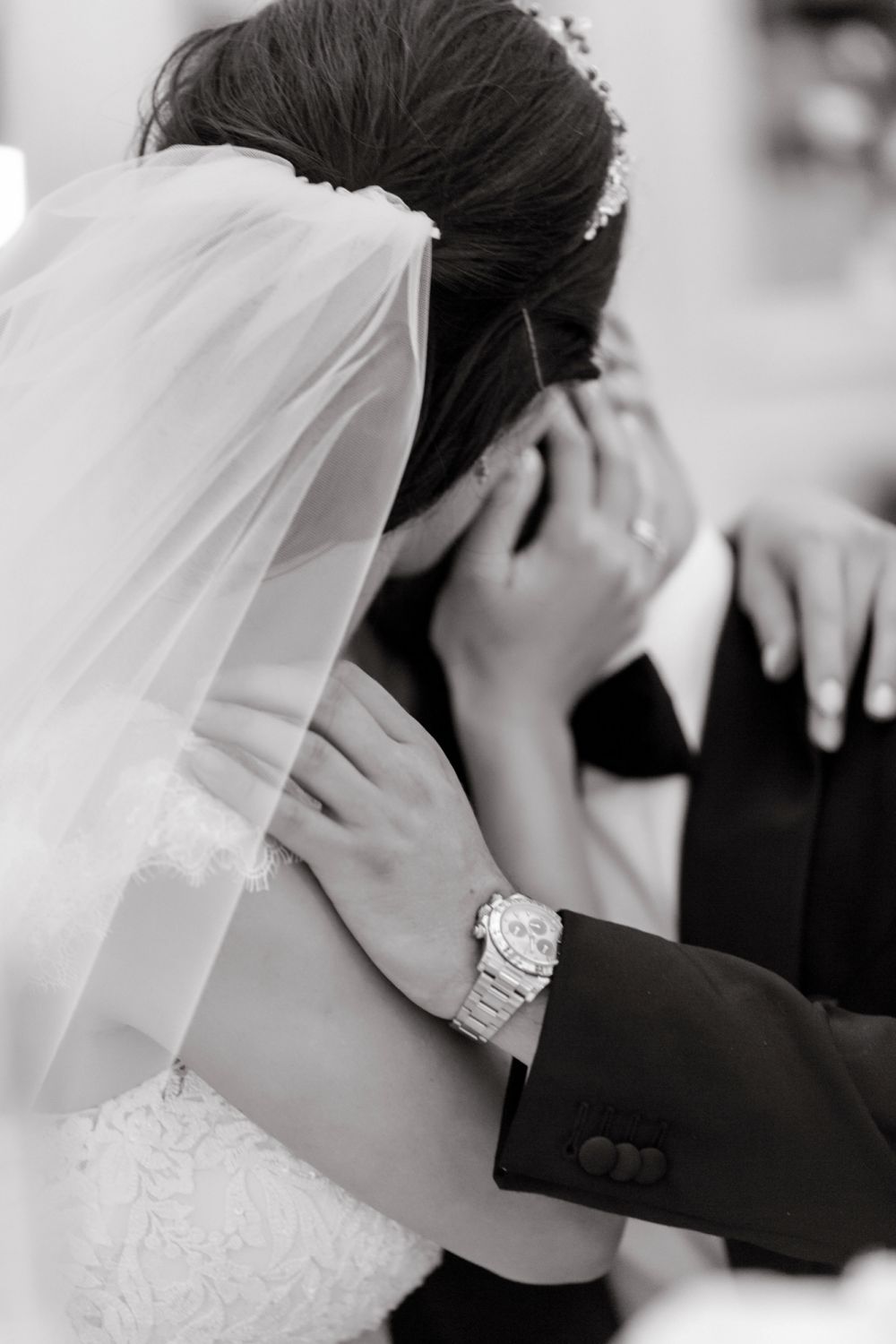 The groom kisses the bride. He hugs her shoulder, their faces hidden by each other