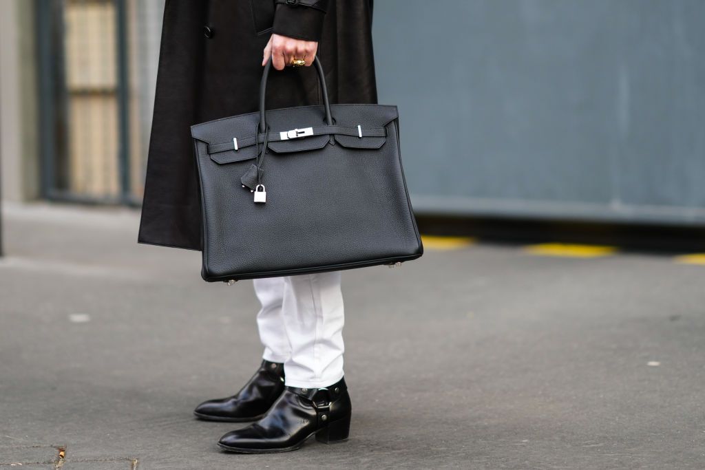 PARIS, FRANCE - JANUARY 22: Pelayo Diaz wears a black shiny leather long coat, gold rings, a black shiny leather large Birkin handbag from Hermes, white denim jeans pants, black shiny leather block heels ankle boot, outside Hermes, during Paris Fashion Week - Menswear F/W 2022-2023, on January 22, 2022 in Paris, France. (Photo by Edward Berthelot/Getty Images)