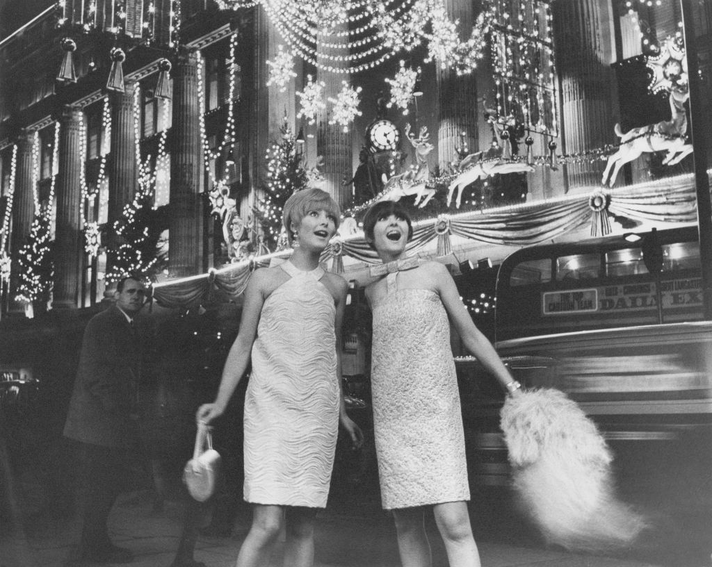 Two models standing outside the Selfridges department store, wearing dresses by French designer Piere Cardin and admiring the Christmas lights on Oxford Street, London, December 1966. The brocade dresses are both exclusive to Miss Selfridge and cost 12 guineas each. (Photo by Evening Standard/Hulton Archive/Getty Images)