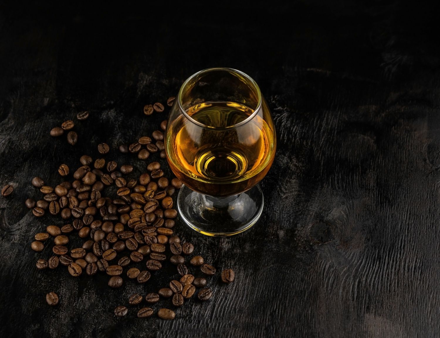 A glass of cognac and coffee beans on a dark wooden background
