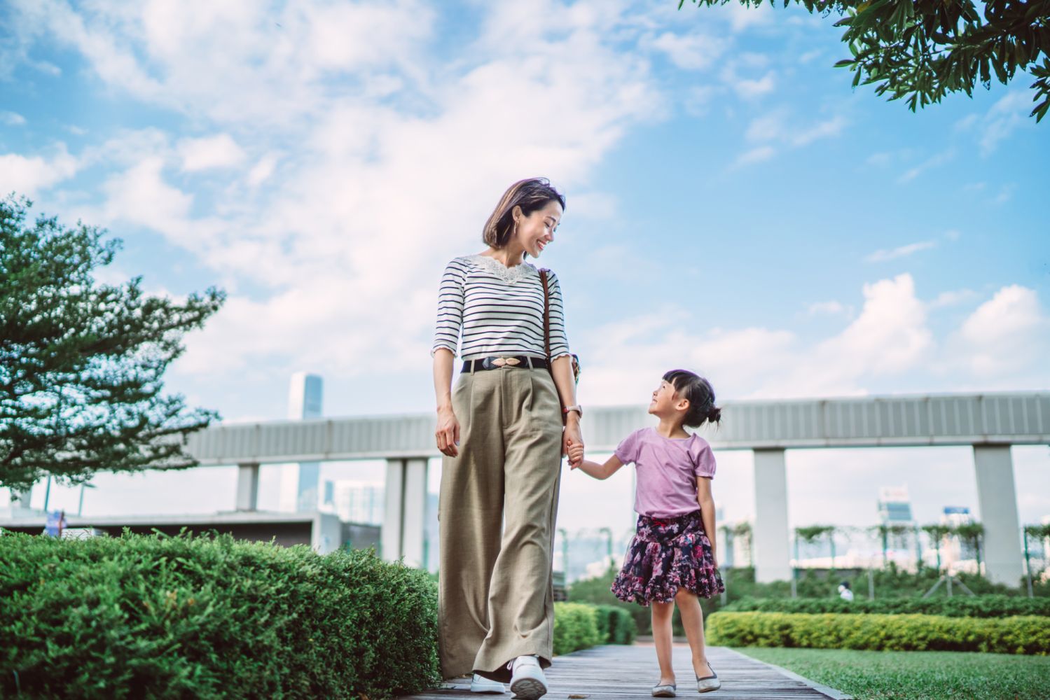 Young pretty mom strolling with her lovely little daughter in park joyfully.