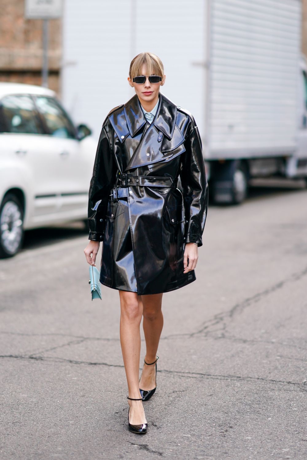 MILAN, ITALY - FEBRUARY 20: A guest wears a black shiny trench coat, a blue Bulgari bag, shoes, outside Max Mara, during Milan Fashion Week Fall/Winter 2020-2021 on February 20, 2020 in Milan, Italy. (Photo by Edward Berthelot/Getty Images)