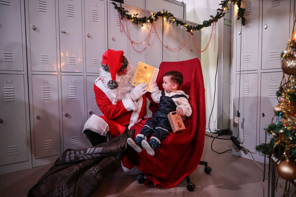 BERLIN, GERMANY - JANUARY 07: A man dressed as Santa Claus hands a gift to a Ukrainian refugee boy at the Tegel refugees registration center and temporary shelter on January 7, 2023 in Berlin, Germany. Over 100,000 refugees from Ukraine have sought shelter in Berlin as Russia's war in Ukraine continues to rage nearly one year on. (Photo by Omer Messinger/Getty Images)
