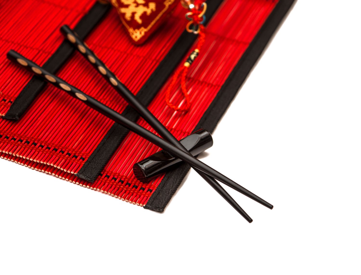 Black chopsticks on red bamboo mat. Asian style table place setting with chinese new years lucky charm