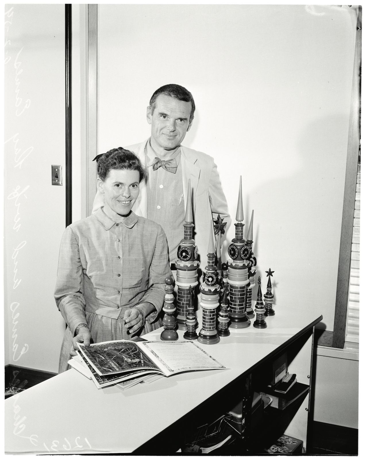 Russian exhibit at press conference, 2 September 1959. Mr and Mrs Charles Eames;watching documentary films;display of Russian toys and books they brought back with them.;Caption slip reads: 'Photographer:Tompkins. Date: 1959-09-02. Reporter: Tompkins. Assignment: Charles Eames exhibit explained at press conf. 70/71: Charles Eames and wife Ray pose in fashion Russian couples stood as they watched documentary film on screens in background. 72/73: Charles and wife Ray Eames display Russian toys and books they