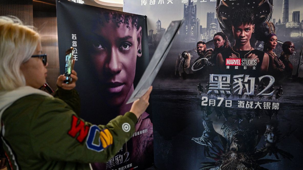 A young woman takes a picture of a poster before watching the movie “Black Panther: Wakanda Forever” at a cinema in Shanghai. Photo: AFP