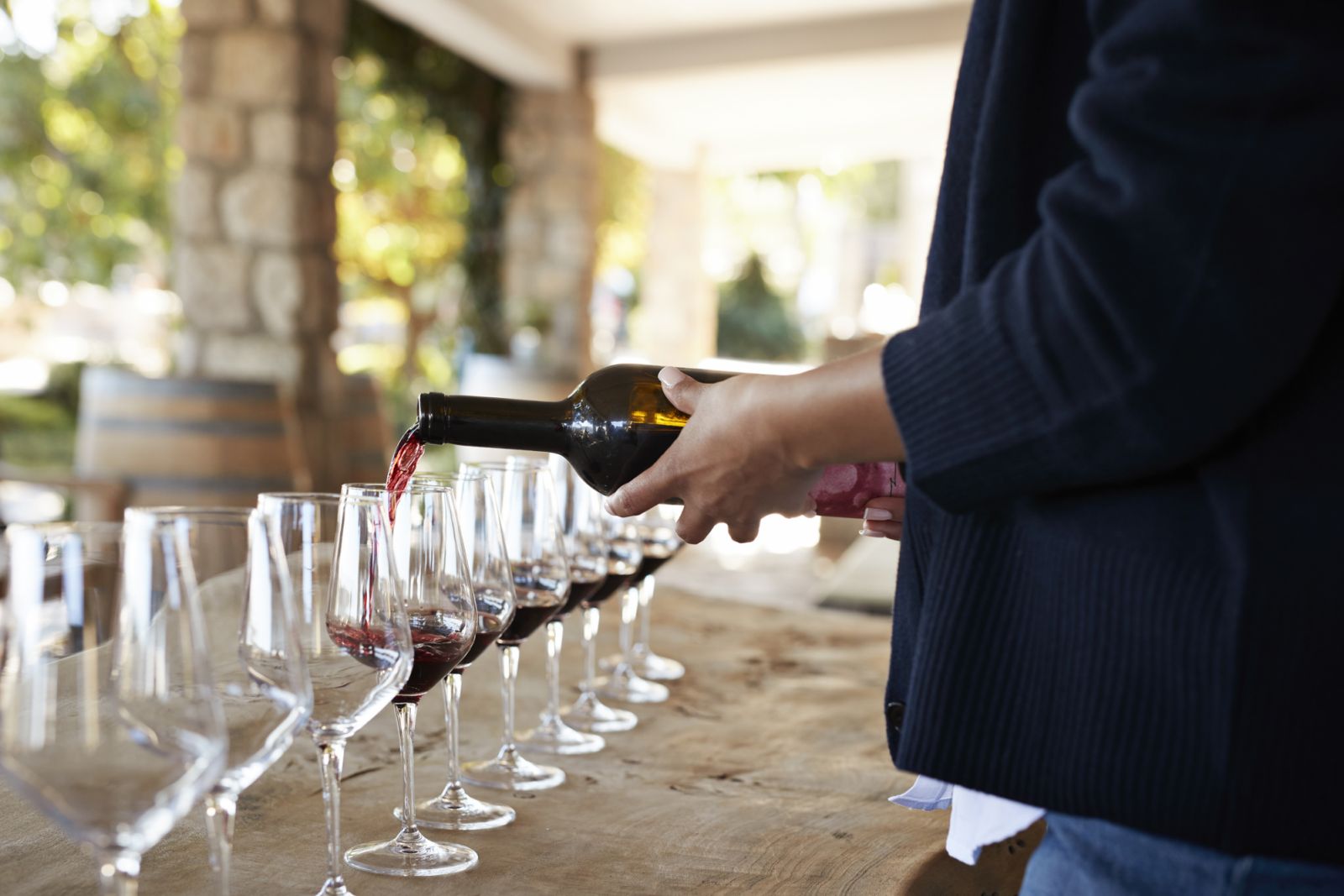 Midsection of entrepreneur pouring red wine in glasses arranged on table