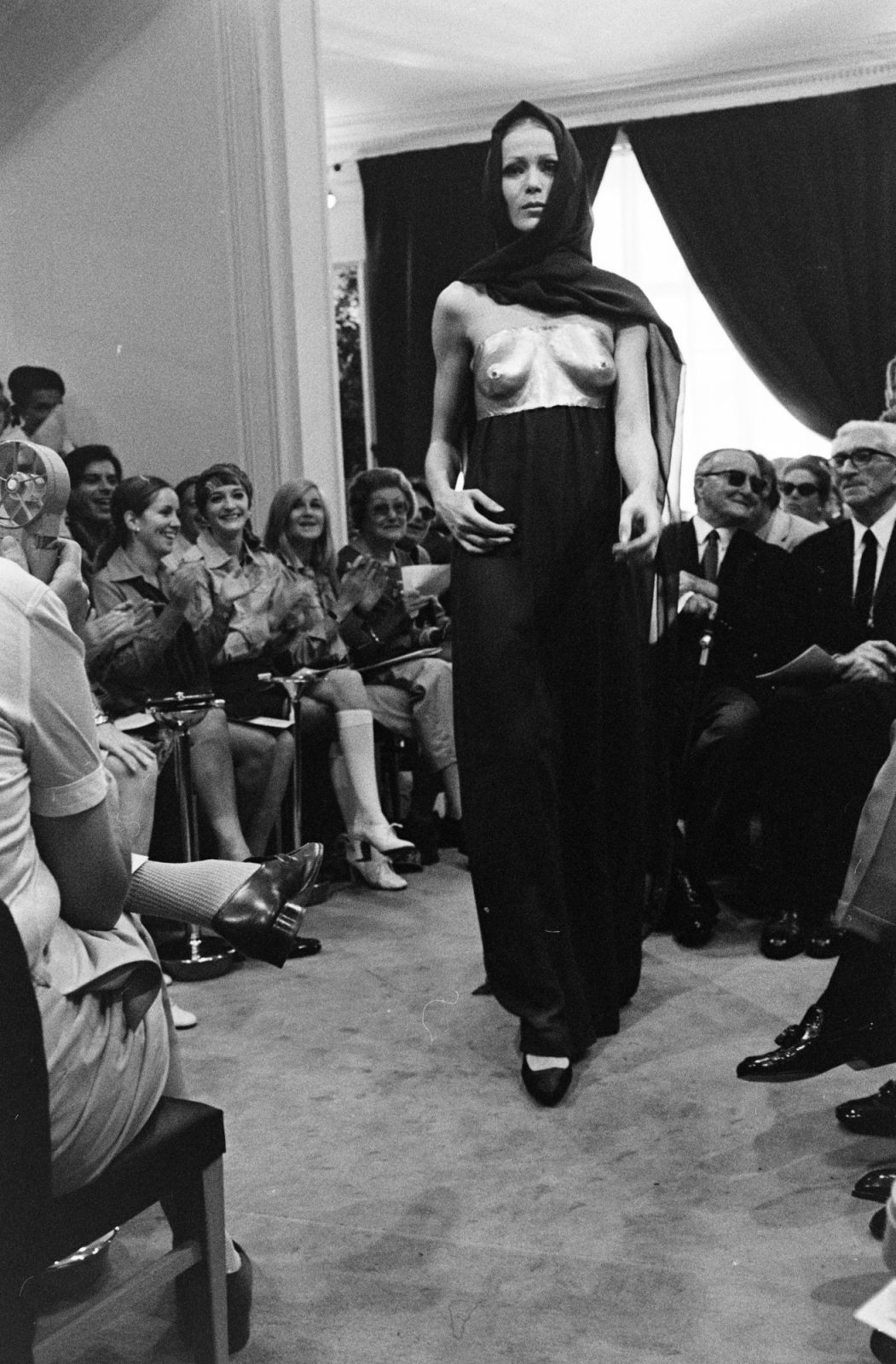 Model Lisa in Yves Saint Laurent's diaphanous chiffon dress worn with artist Claude Lalanne's copper cast of model Veruschka's body during his fall 1969 Haute Couture collection presentation. Lou Lou de la Falaise and Betty Catroux observe from the front row. (Photo by Reginald Gray/WWD/Penske Media via Getty Images)