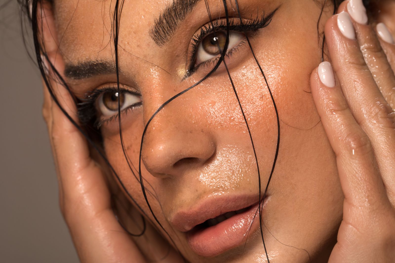 Close up studio shot of a beautiful brunette woman with glowing skin. Holding hands near her face.