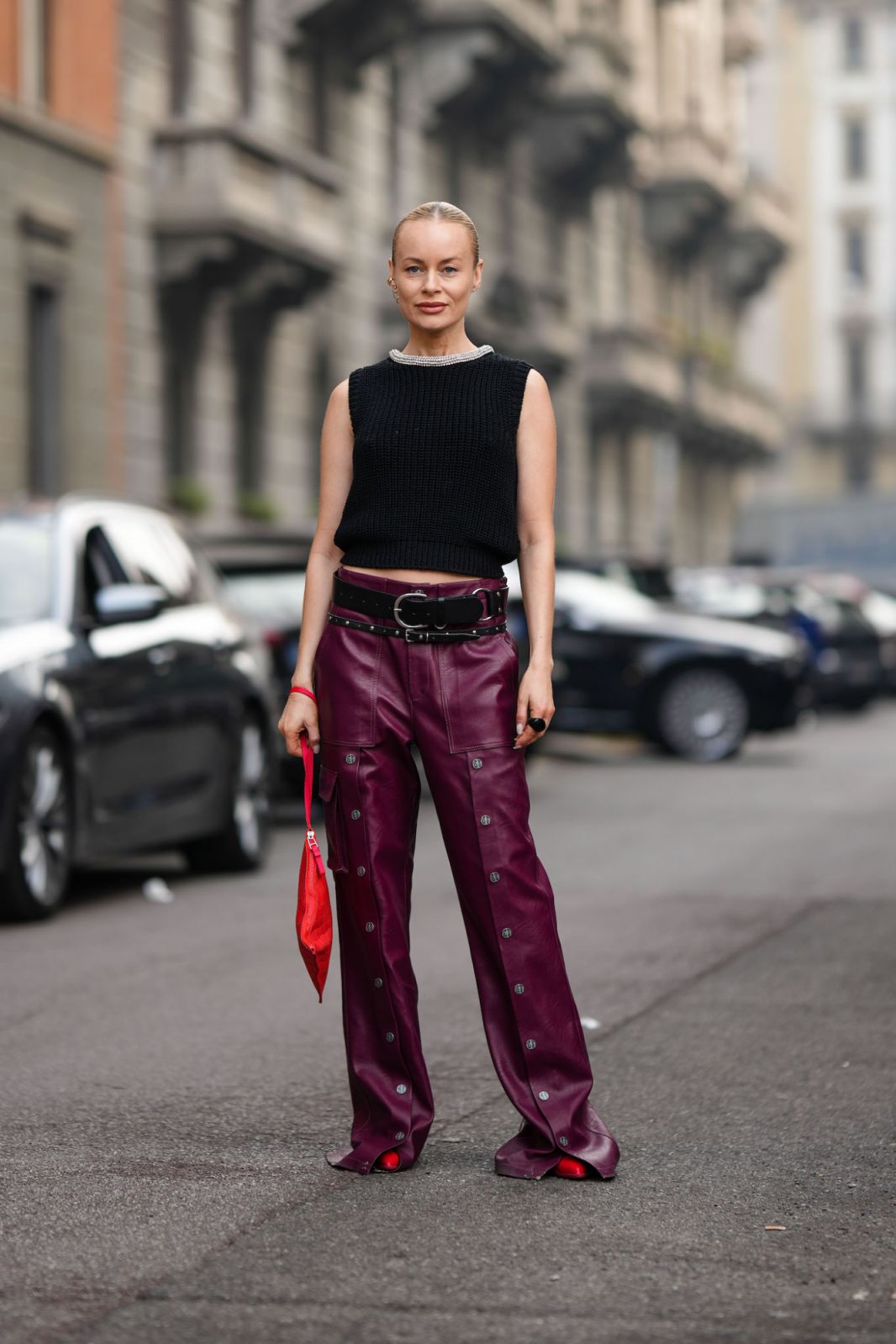 MILAN, ITALY - FEBRUARY 23: Thora Valdimars wears a rhinestones large necklace, a black sleeveless braided wool tank-top, a black shiny leather nailed / studded belt, purple shiny leather nailed / studded wide legs pants, a red shiny leather braided handbag, red shiny leather pointed pumps heels shoes , outside Max Mara, during the Milan Fashion Week Womenswear Fall/Winter 2023/2024 on February 23, 2023 in Milan, Italy. (Photo by Edward Berthelot/Getty Images)
