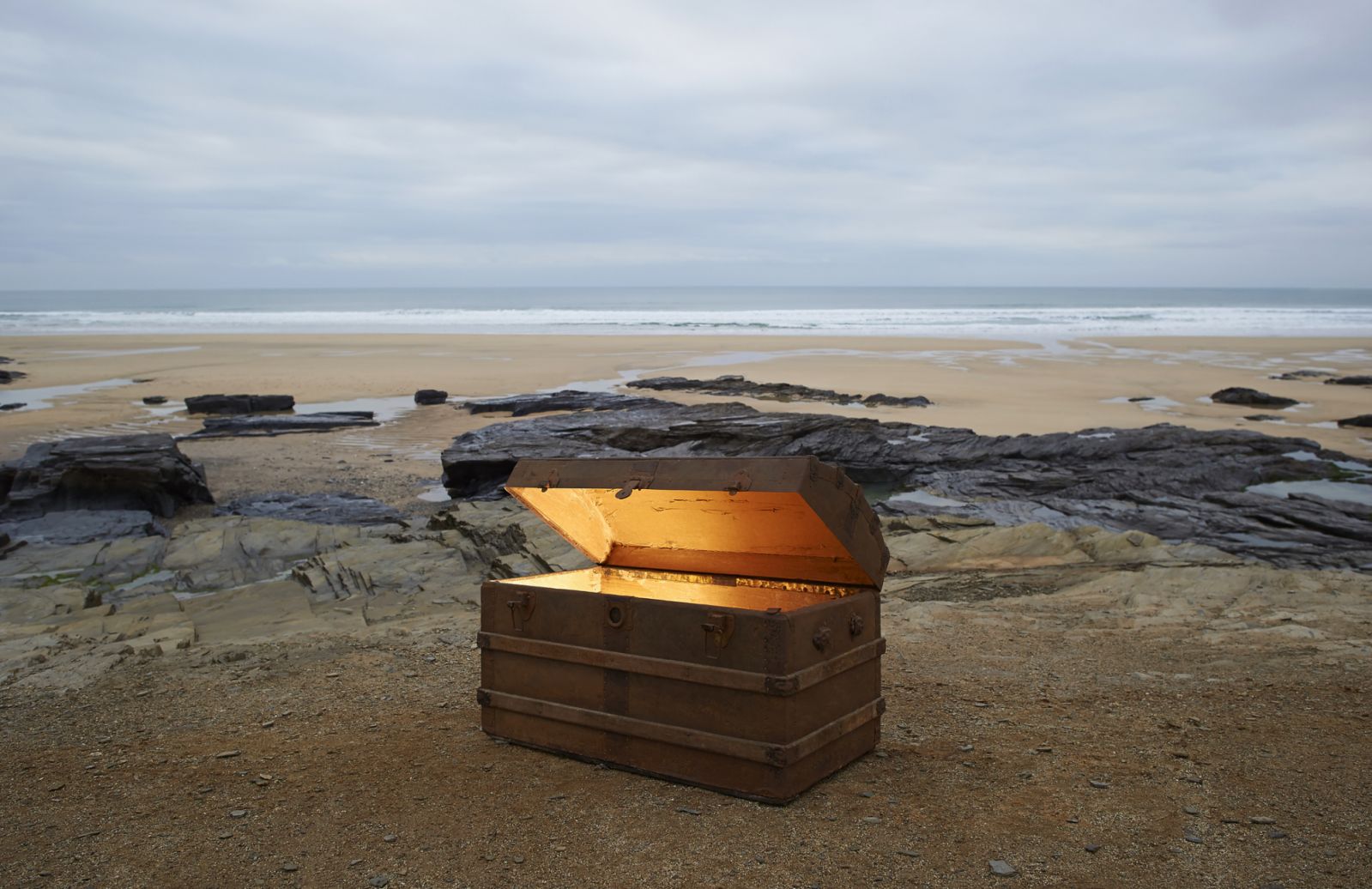 An open treasure chest with golden light from inside on a deserted beach. A treasure chest full of gold.