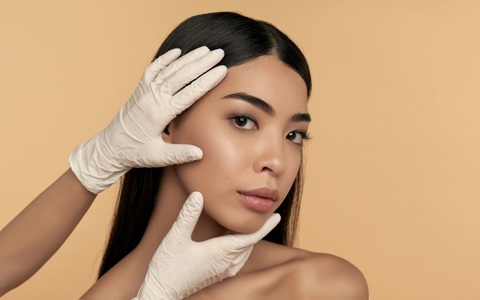 Young Asian woman with clean radiant skin gets botox injections for contour tightening, lip augmentation on a beige background. Spa care, facial skin care, beauty cosmetology.