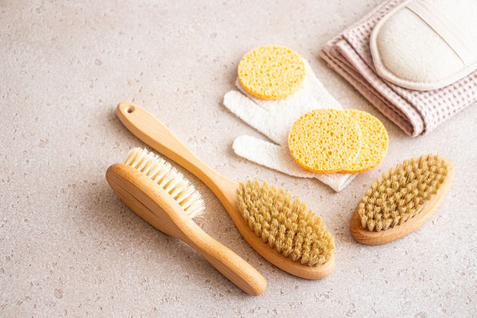 Close-up of wooden dry skin body brushes, cleaning sponges, cleaning mitten, serum bottles on concrete background, selective focus. Spa at home, flat lay. Zero waste concept