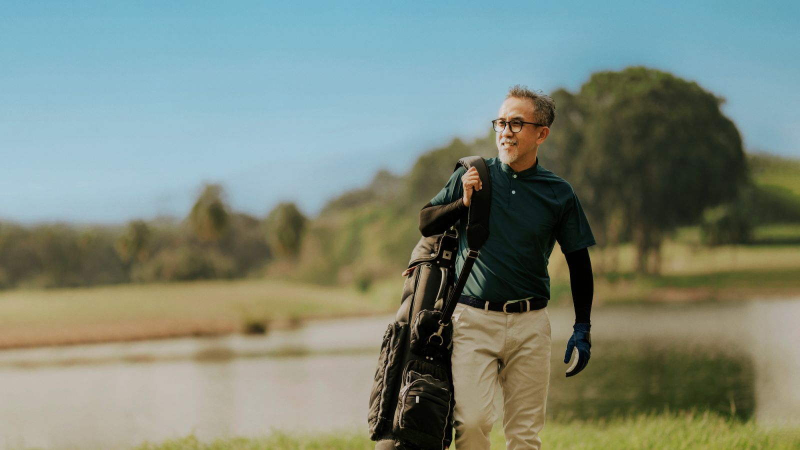 side view of a matured man golfer carrying a golf bag looking away in the golf course