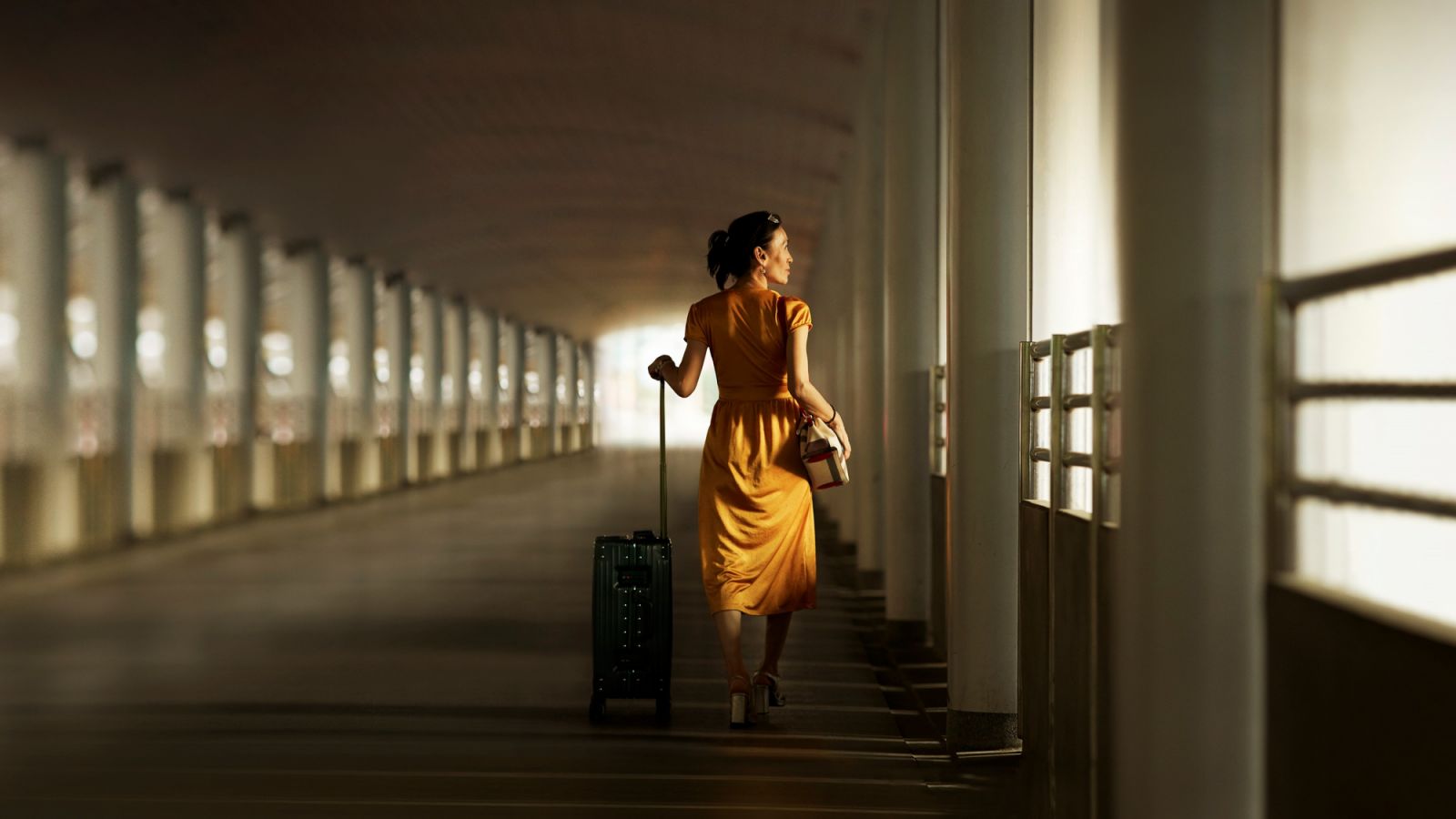 Full length rear view of woman with luggage walking on bridge at railroad station