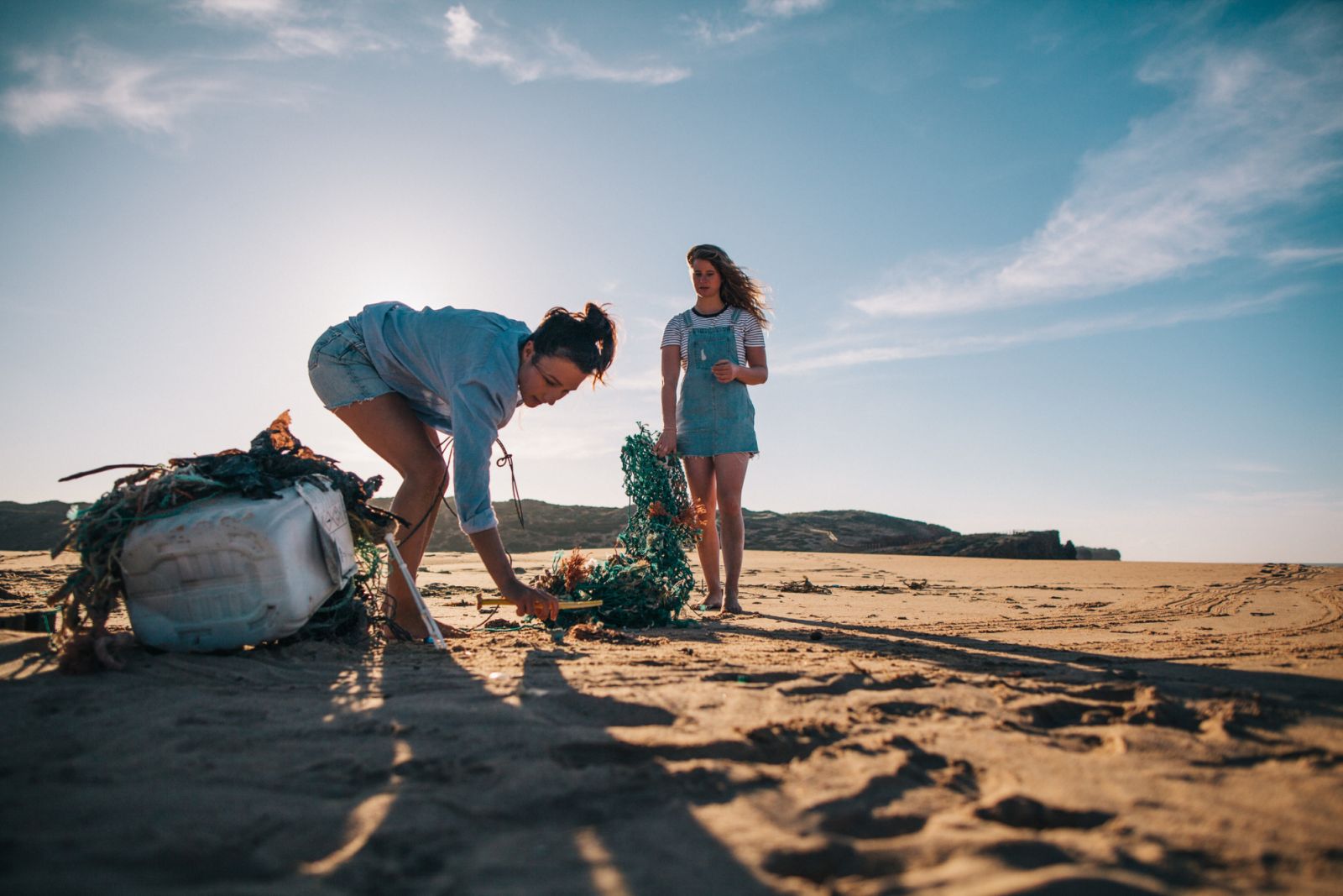 Two women cleaning up the beach collecting plastic and fishing nets / Algarve, Portugal. Part of a series.