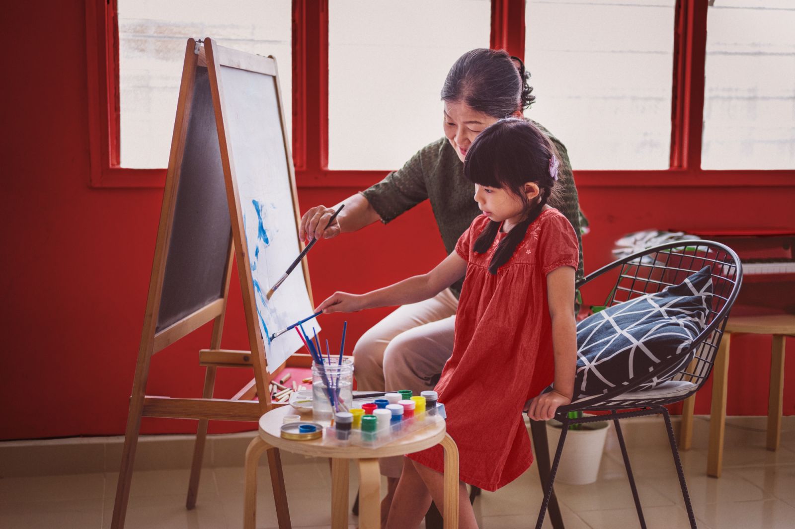 An Asian grandmother painting with her granddaughter at living room.