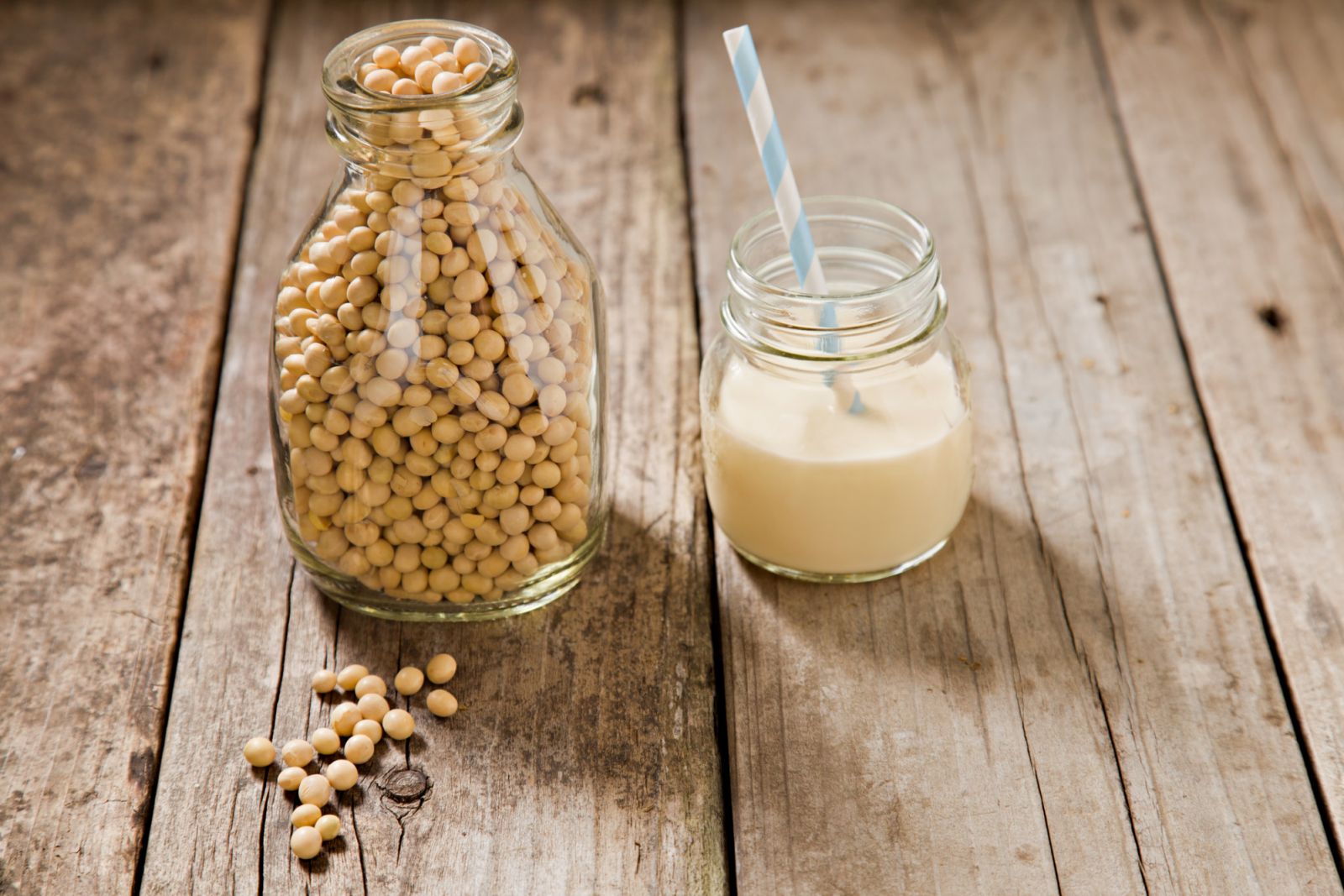 A close up shot of an old milk bottle filled with dry soy beans with a few beans on the foreground and a small glass jar container with soy milk and a straw (Photo: Getty Images)