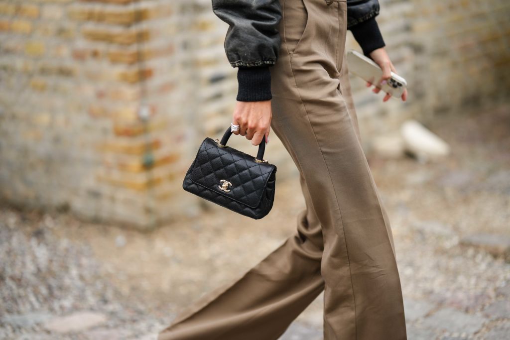 COPENHAGEN, DENMARK - AUGUST 10: A guest wears a black faded leather bomber coat, a black shiny leather shoulder bag from Chanel, brown high waist / flared pants, outside Munthe, during the Copenhagen Fashion Week Spring/Summer 2024 on August 10, 2023 in Copenhagen, Denmark. (Photo by Edward Berthelot/Getty Images)