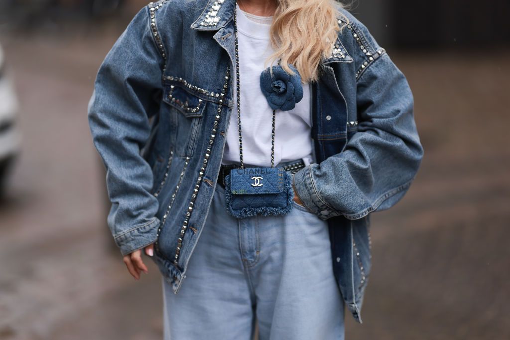 COPENHAGEN, DENMARK - AUGUST 09: Guest seen outside Skall Studio show wearing white headscarf with blue writings, distressed denim jacket with studs added, denim Chanel crossbody bag with a denim flower as a added detail, washed out pair of jeans and  white leather ballet flats with studs during the Copenhagen Fashion Week Spring/Summer 2024 on August 09, 2023 in Copenhagen, Denmark. (Photo by Jeremy Moeller/Getty Images)